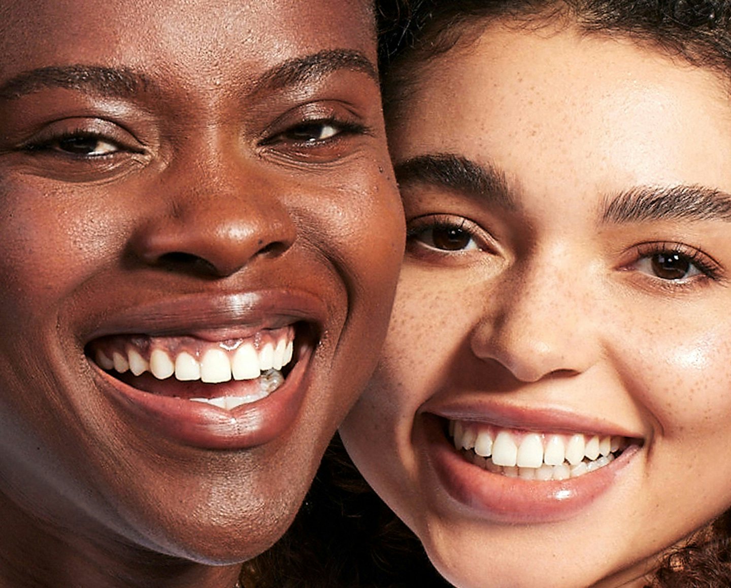 Two smiling women, with light and dark skin tones, wearing Neutrogena's invisible sunscreen and ultra sheer sunscreen without a visible white cast.